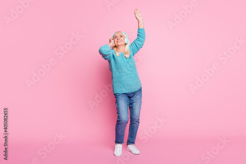 Full length photo of retired woman dance look up empty space wear blue sweater jeans earphones footwear isolated pink color background