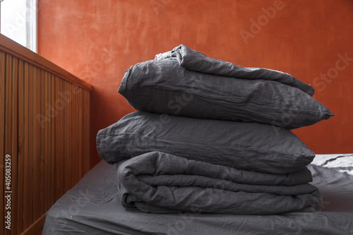 A stack of plain pillows, blankets on the bed. Gray linens on red wall background © Ольга Альперович