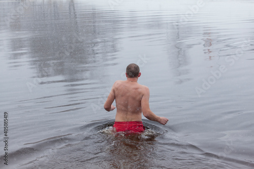 Man entering the icy water of a winter river in water baptism in the Orthodox tradition. Dnieper. Kiev. Ukraine