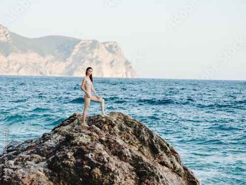 woman stands on a high rock in nature near the sea and a mountain in the backgroun © SHOTPRIME STUDIO