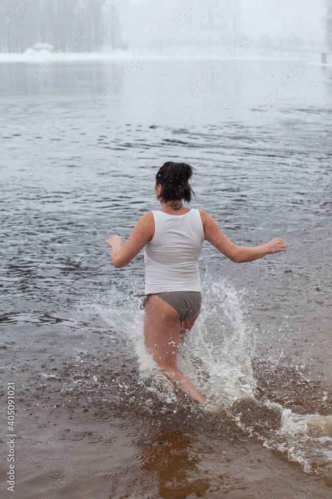 Fototapeta premium Swimming in the winter. Woman enters ice bathing water