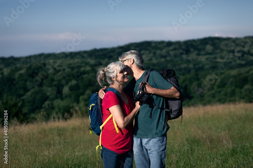 Active senior couple with backpacks hiking in nature .