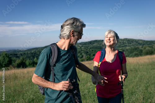 Active senior couple with backpacks hiking in nature .