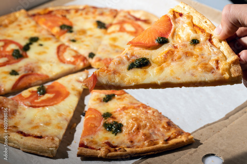 Woman hand taking salmon pizza slice from box. Pizza in hand, close up. Meal time at office