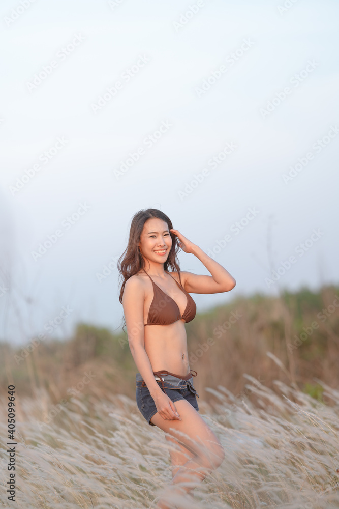 Beautiful blonde women in a brown bikini on a brown meadow with white flowers in the summer evenings.