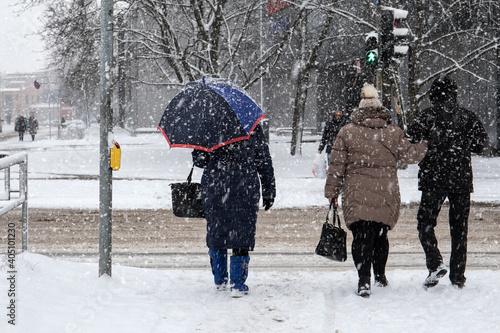 Fototapeta Naklejka Na Ścianę i Meble -  In snowstorm people cross the street. Winter, frost and urban environment