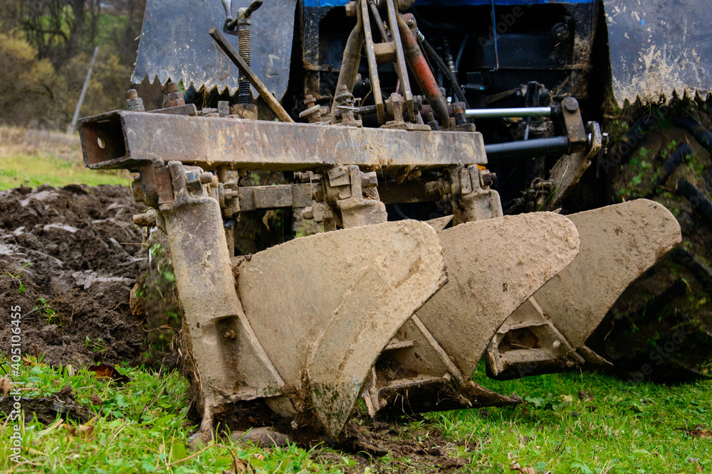 Fototapeta premium Land cultivation,tractor plows the ground, a blue small tractor and a plow with three knives.