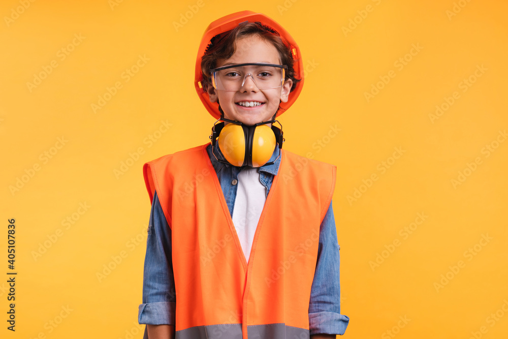 Portrait of a young boy future construction worker in orange uniformn isolated over yellow background Portrait of a young boy future construction worker in orange uniformn isolated over yellow background