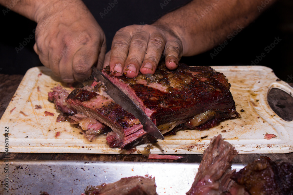 Smoked beef rib being sliced ​​with a knife. Slices with a slight pink color indicating smoke to the point. Rustic food made on the grill and smoked at Pit Smoker. Cutting meat. Gastronomy. Gourmet.