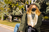 Woman sitting on a park bench with her back to a man with surgical mask