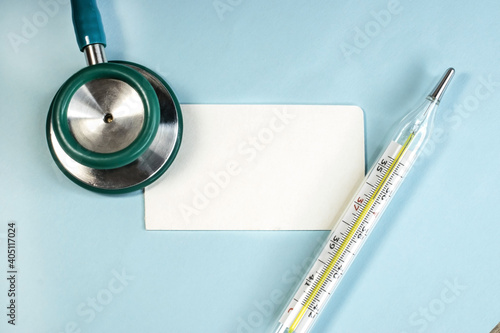 Ampoule with red medicine pills stethoscope briefcase on glass tableOn a blue background among a stethoscope and a mercury thermometer lies a white blank sheet for notes. The concept of health photo