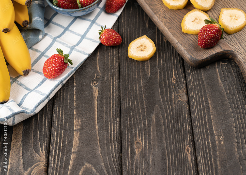 Slised banana and strawberries on a wooden board close up
