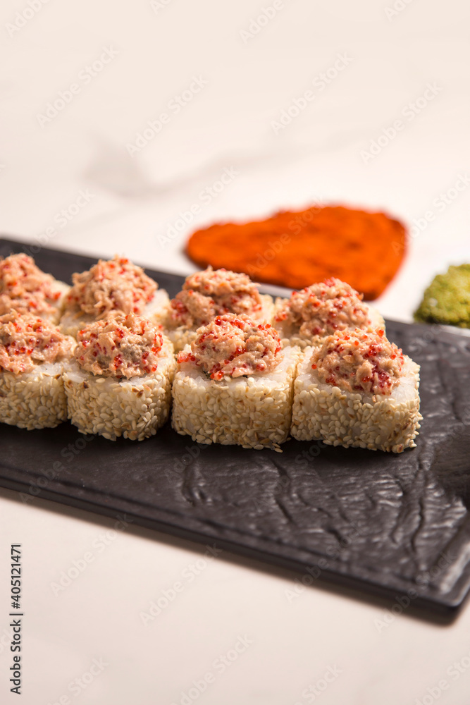 Close up of Japanese sushi roll with roasted salmon and tobiko flying fish roe on top served on black plate. heart shapes of turmeric and basil spices on marble background. Asian menu dish
