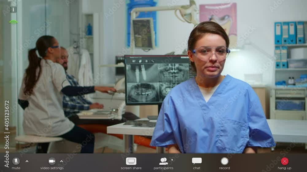 Dental assistant explaining to patients the importance of oral hygiene looking at camera in dental center. Stomatologist nurse speaking on webcam, footage with software overlay concept Dental assistant explaining to patients the importance of oral hygiene looking at camera in dental center. Stomatologist nurse speaking on webcam, footage with software overlay concept