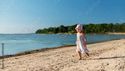 childhood, leisure and people concept - happy little baby girl running along summer beach