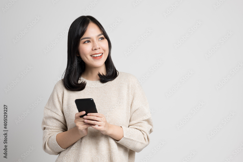 Beautiful young asian woman holding smartphone standing on isolated white background. She is looking at blank space and thinking something. Beautiful young asian woman holding smartphone standing on isolated white background. She is looking at blank space and thinking something.