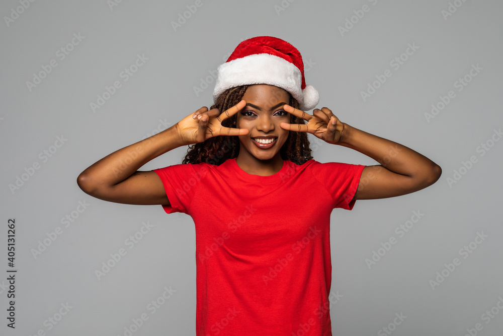 Beautiful african woman in santa hat with v-sign gesture on grey background