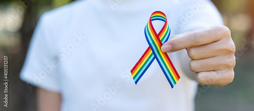 hand showing LGBTQ Rainbow ribbon against sky background in the morning. Support Lesbian, Gay, Bisexual, Transgender, Queer community and Rights concept