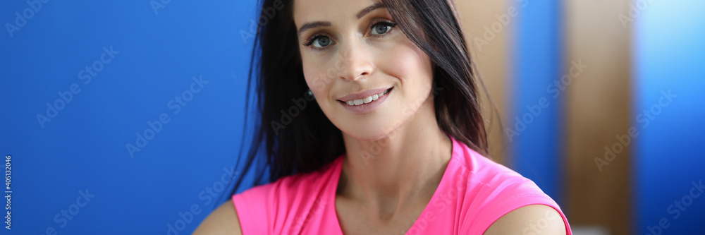 Portrait of charming smiling female wearing pink sportswear. Brunette pretty woman in yoga studio. Bright blue wall. Healthy lifestyle and sport activity concept Portrait of charming smiling female wearing pink sportswear. Brunette pretty woman in yoga studio. Bright blue wall. Healthy lifestyle and sport activity concept