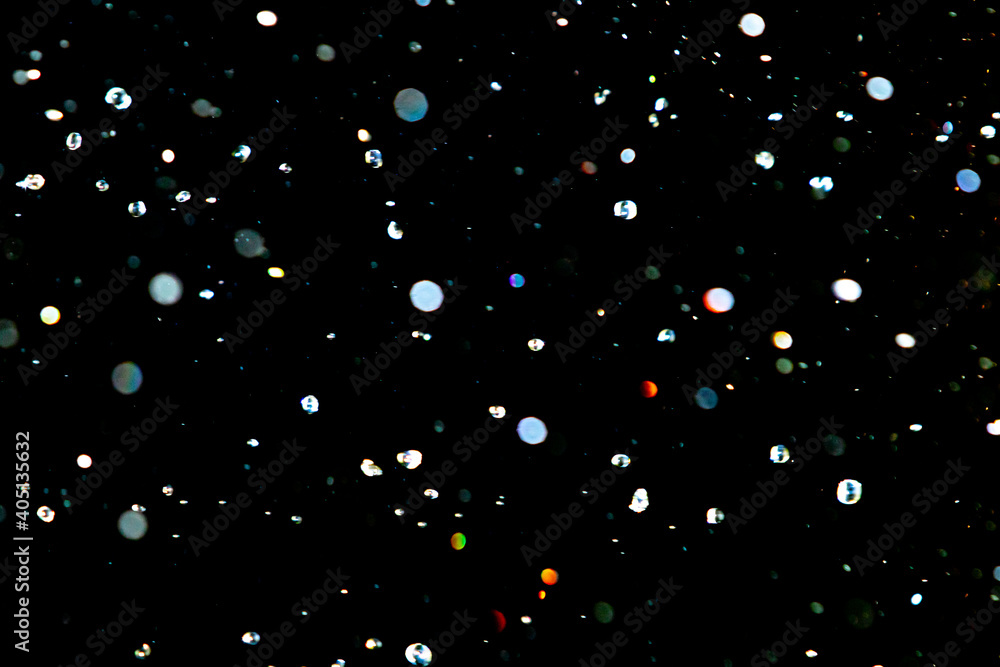 Bright spots of bokeh, drops of water on a black background, out of focus.
