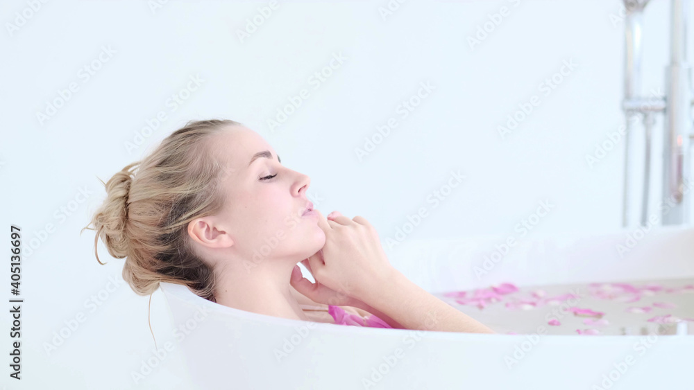 Beautiful Caucasian Blonde Girl In Bikini Lying In Flower Bath In Resort Day Spa Salon. Skin Care Therapy. Concept young woman relaxing in the bathtube. Beautiful Caucasian Blonde Girl In Bikini Lying In Flower Bath In Resort Day Spa Salon. Skin Care Therapy. Concept young woman relaxing in the bathtube.
