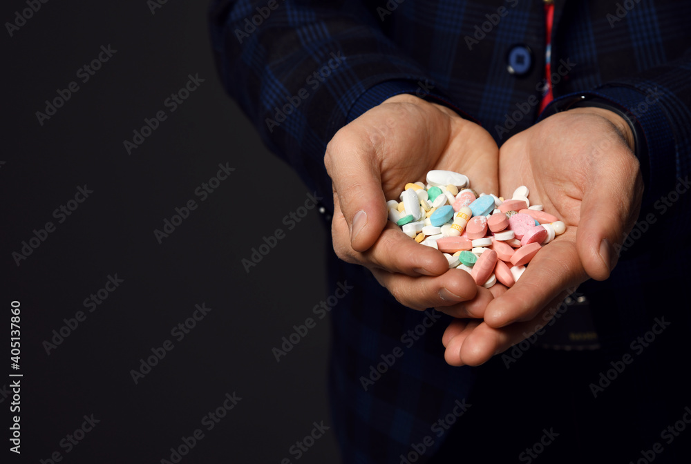 Closeup of heap of colorful medical pills in man hands in checkered jacket over dark background with copy space. Drugs, medicare, healthcare concept