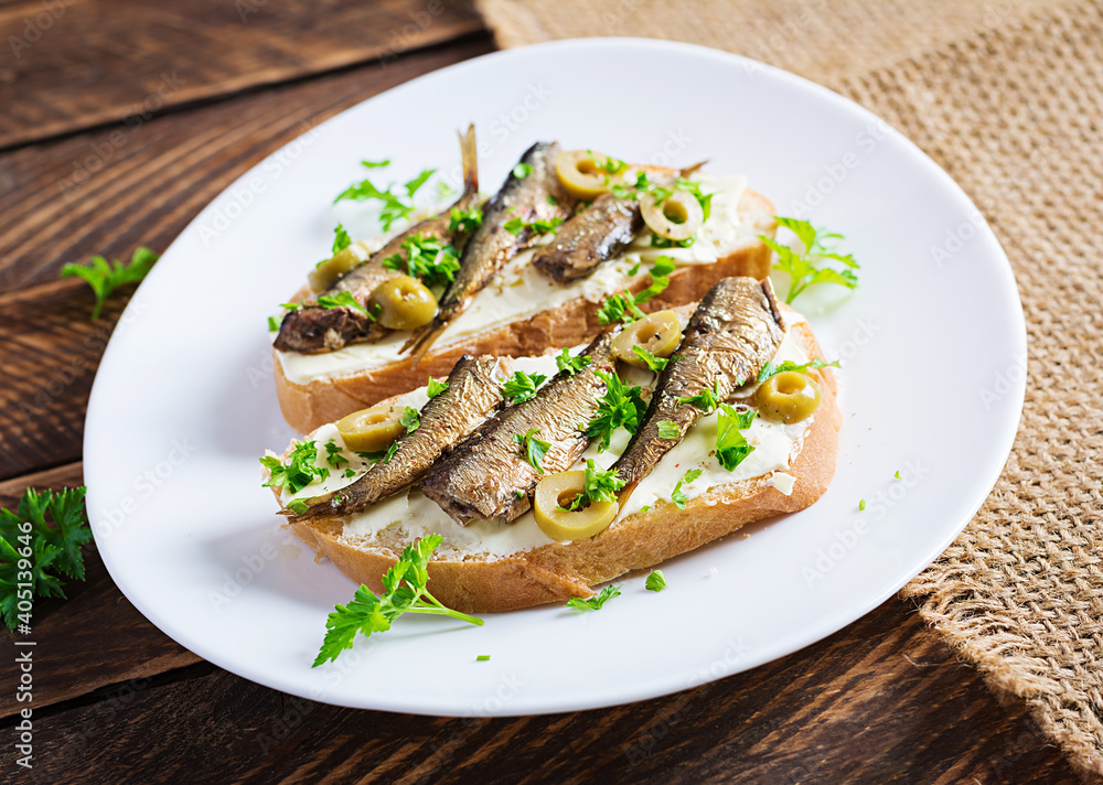 Sandwich - smorrebrod with sprats, green olives and butter on wooden table. Danish cuisine.
