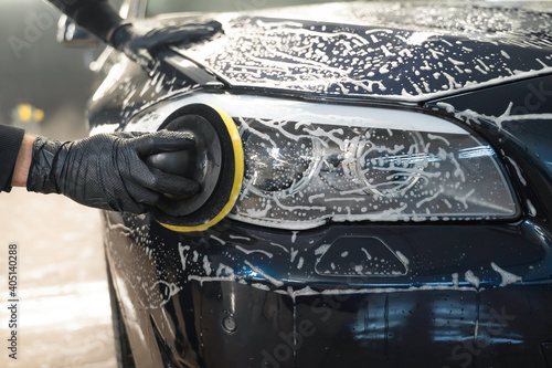 Man cleans car lamp with circle sponge. Preparing auto for polishing. Detailed car wash