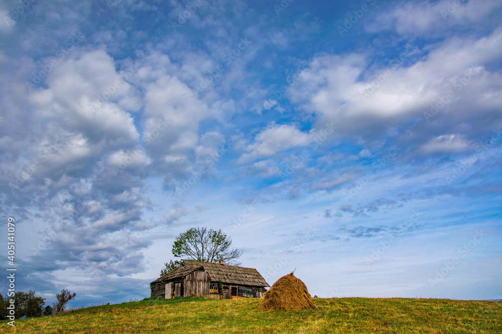 Haystack, mountain wooden hut and lonely tree on top of the hill under the picturesque sky, Borsa, Maramures, Romania Haystack, mountain wooden hut and lonely tree on top of the hill under the picturesque sky, Borsa, Maramures, Romania