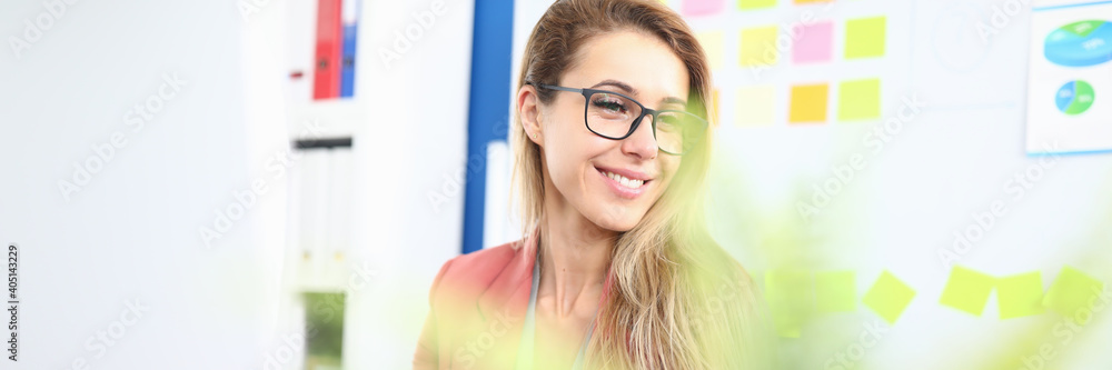 Portrait of smiling charming young woman at work place. Happy cute female working in financial company. Green plant on table. Business and career success concept