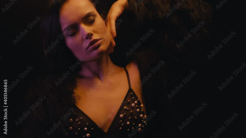 brunette woman in bra and faux fur coat adjusting hair on black brunette woman in bra and faux fur coat adjusting hair on black