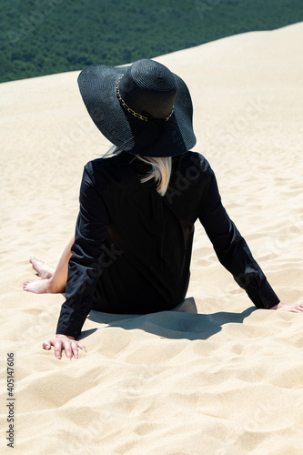 girl on a sand dune in a black hat and a beautiful forest view photo