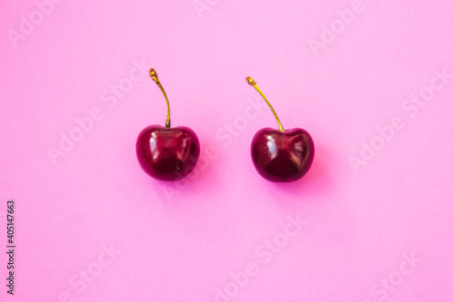 Two ripe cherries on bright neon pink background. Valentine's Day concept. Close-up of cherries. Summer background