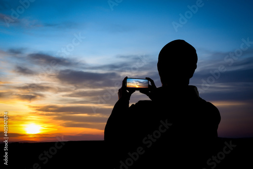 Silhouette of young man shoots sunset on phone, smartphone. Travel, walking.