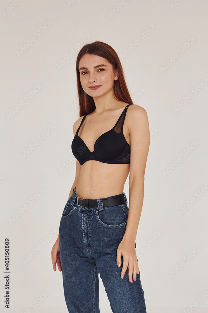 Young woman in jeans and bra indoors. White background Young woman in jeans and bra indoors. White background