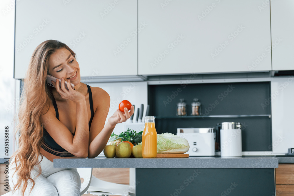 Talks by the phone. Young european woman is indoors at kitchen indoors with healthy food Talks by the phone. Young european woman is indoors at kitchen indoors with healthy food