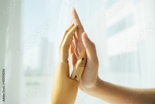 Hand of wooden cyborg robot and human touching each other.