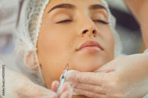 therapists hands in gloves with syringe and cotton pad making filler injection in womans underlip