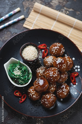 Black plate with asian-style teriyaki sauce meatballs, high angle view on a brown stone surface, vertical shot