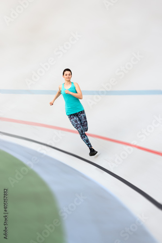 Sporty young woman running by all-season track at the city stadium.