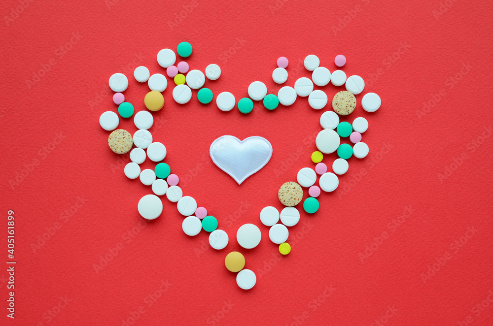 Many different tablets in the shape of heart and white heart on a red background. Medical flat lay . Valentine's Day.