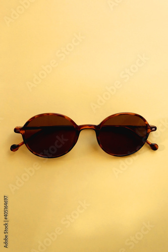 Round brown sunglasses on pastel yellow background. Top view.