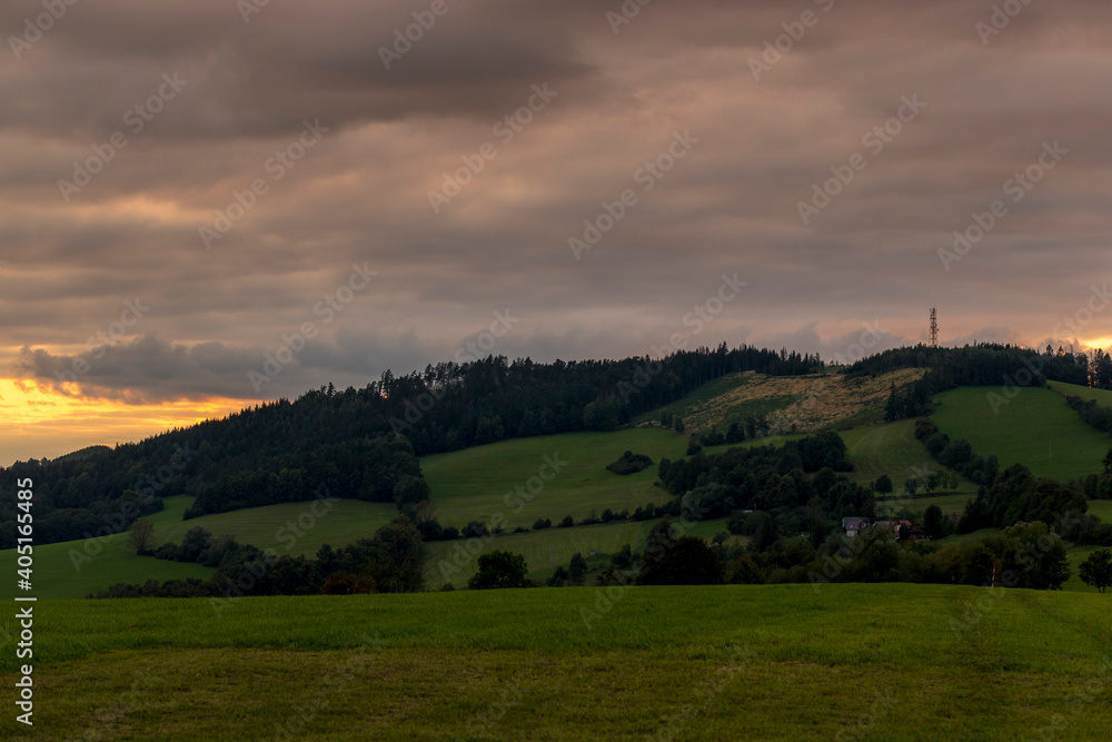 Obraz premium Sunset over mountains and hills with colorful clouds on the horizon that spill from side to side in orange.