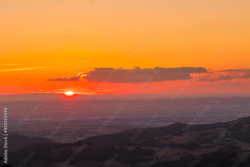 Fototapeta premium A view of a landscape full of mountains during a golden sunset with the sun on the horizon and a view of the sun from the top of Mount Ondrejnik.