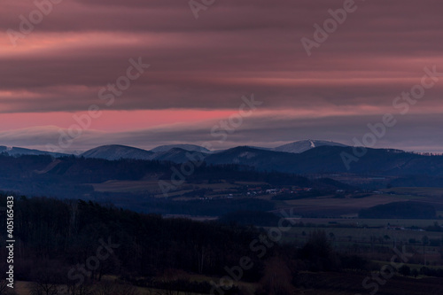 Sunset dark sky with clouds over the mountainous landscape of Pustevny lying under the fog in a dark color. © Lukas