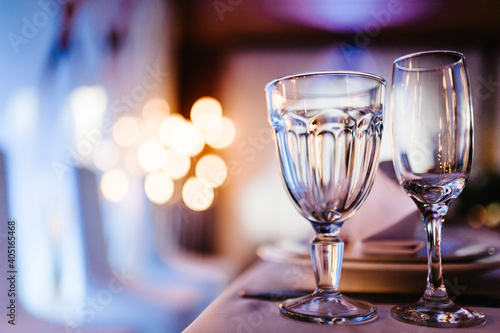 Close up picture of empty glasses in restaurant and cutlery. Silverware or flatware on plates, glasses for champagne and wine glasses. Reflection, bokeh and bright light.