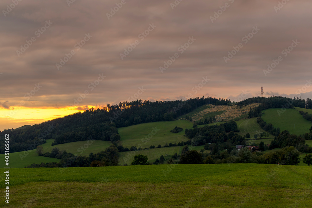 Fototapeta premium Sunset over mountains and hills with colorful clouds on the horizon that spill from side to side in orange.