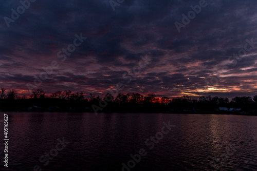The water surface of the lake during a colorful sunset with the reflection of the surrounding tree on the water surface.