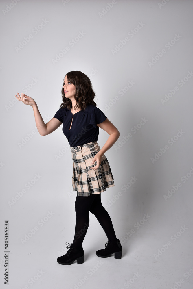 Full length portrait of pretty brunette woman wearing tartan skirt and blouse. Standing pose on the ground, against a studio background. Full length portrait of pretty brunette woman wearing tartan skirt and blouse. Standing pose on the ground, against a studio background.