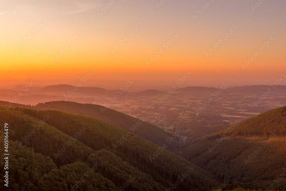 A detailed view of the sun as it changes from yellow to red and slowly sets behind the mountainous area of the Beskydy Peaks and the surrounding nature.